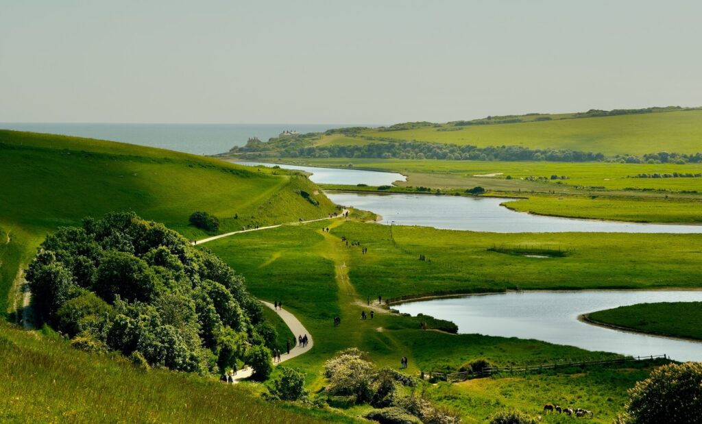 View across the Seven Sisters Country Park showing the winding Cuckmere River, green fields and walking paths leading towards the sea.